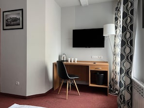 Quarto de hotel com secretária de madeira, cadeira preta e televisão de tela plana na parede.
