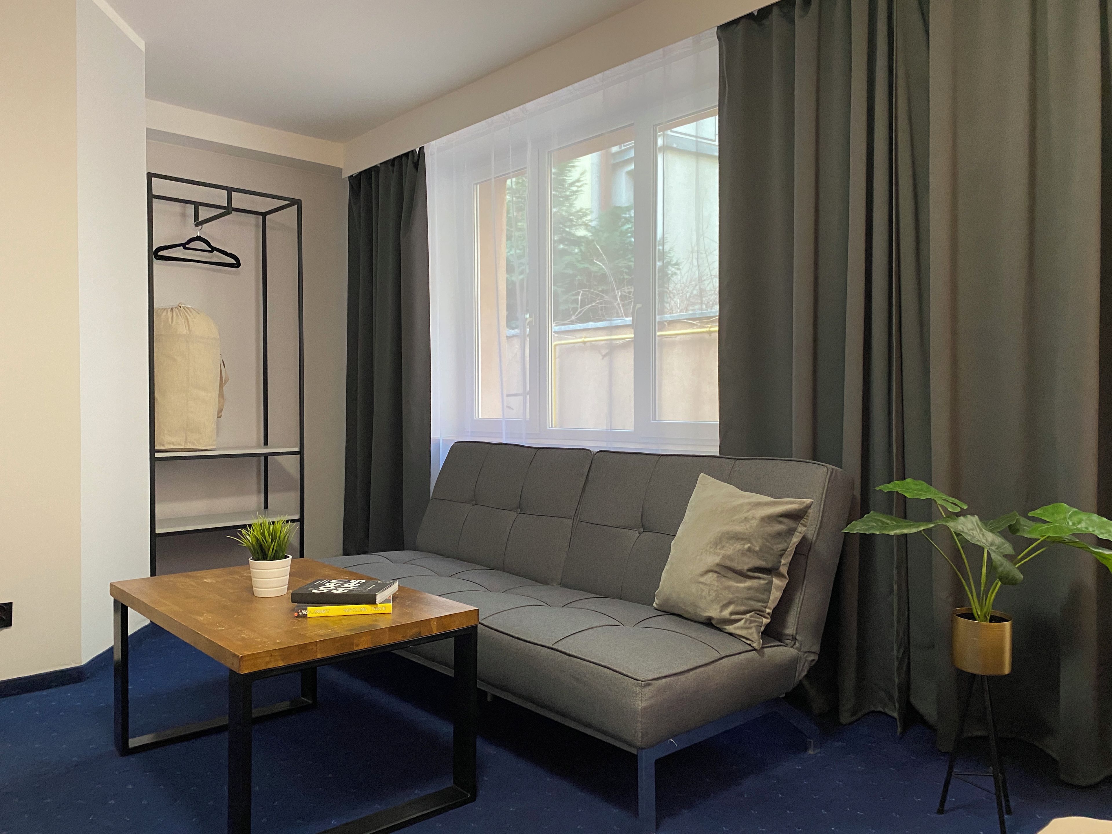 Una sala de estar moderna con un sofá gris, una mesa de centro de madera, un armario suspendido y una ventana con cortinas.