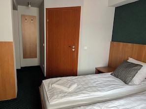 Une chambre d’hôtel avec une porte en bois, un lit avec une literie blanche, une table de chevet et un mur d’accent vert.