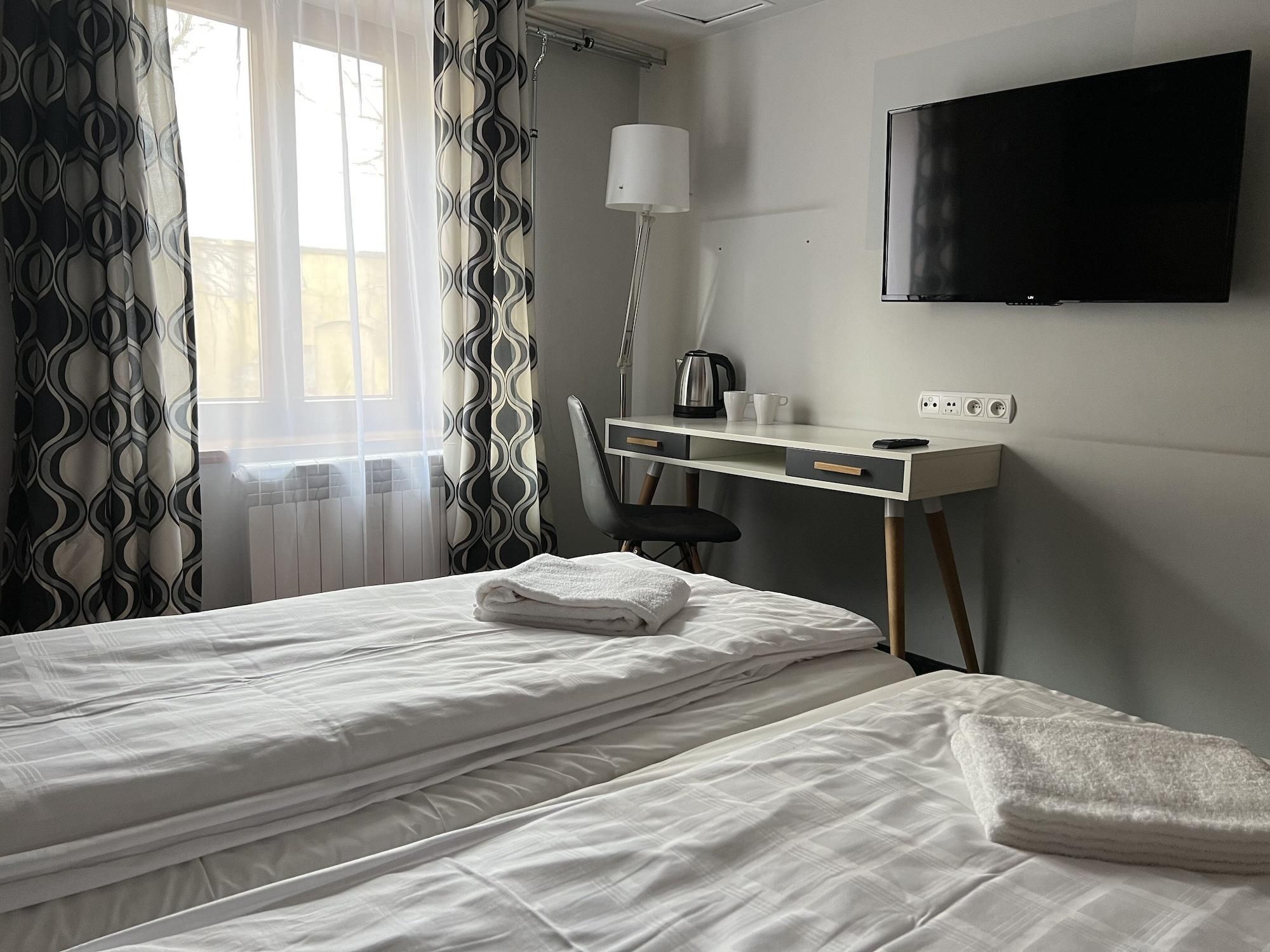 Een hotelkamer met twee bedden, een bureau, een stoel, een televisie en een raam met gordijnen.