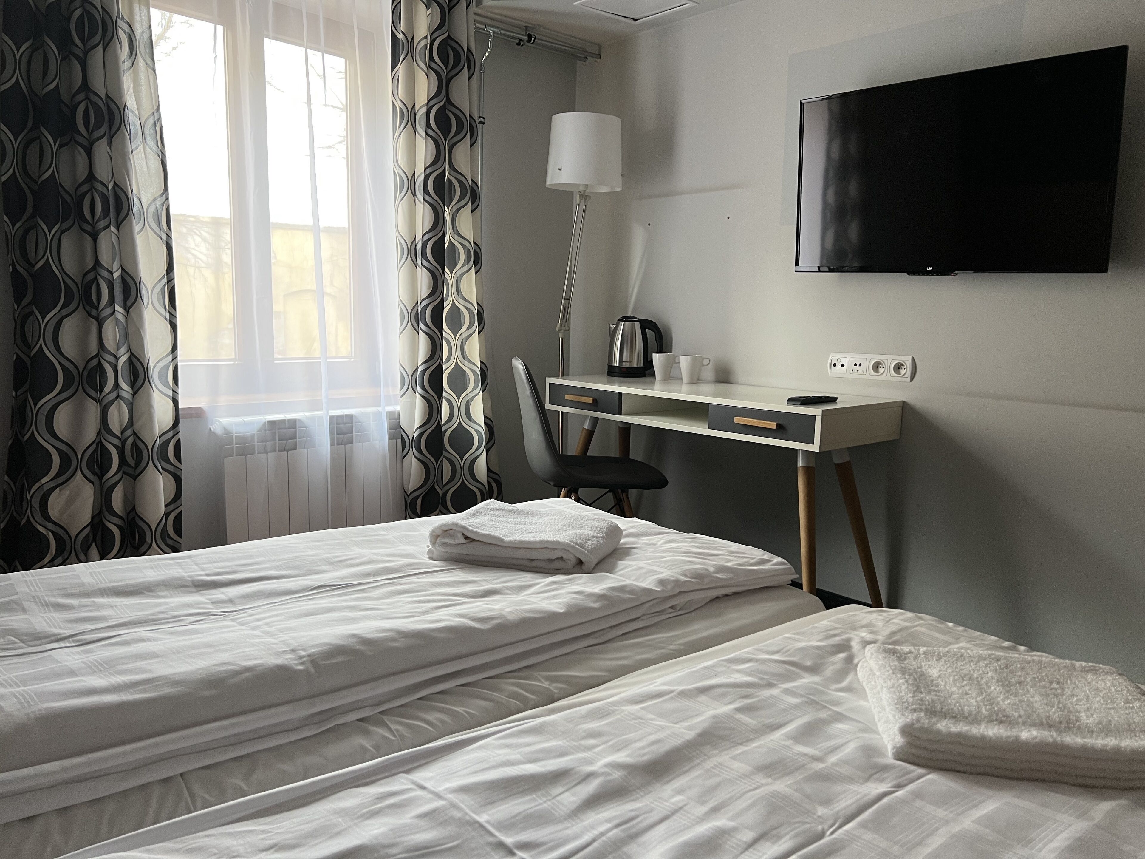 A hotel room with two beds, a desk with a chair, a TV, and a radiator.