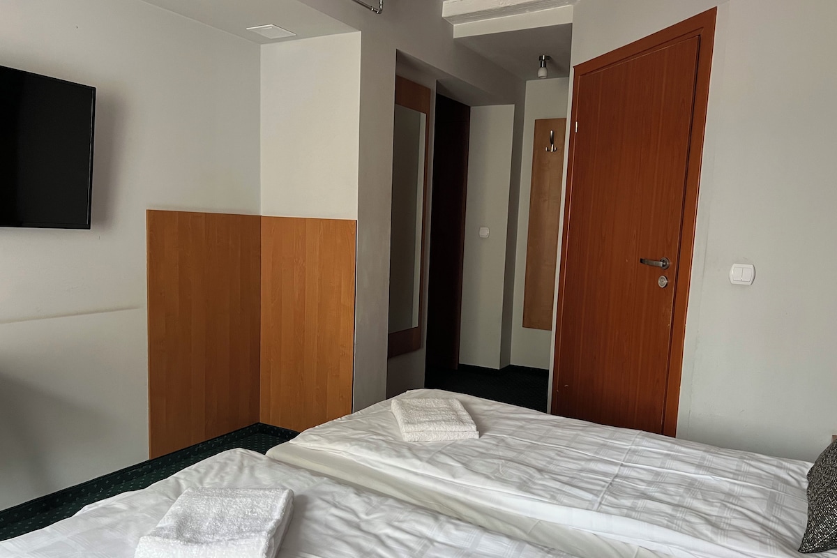 Quarto de hotel com uma cama, um guarda-roupa de madeira, um espelho e uma televisão na parede.