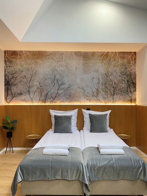 Une chambre d’hôtel moderne avec un grand lit, deux oreillers, une table de chevet et un tableau représentant des arbres sans feuilles, accroché au mur.