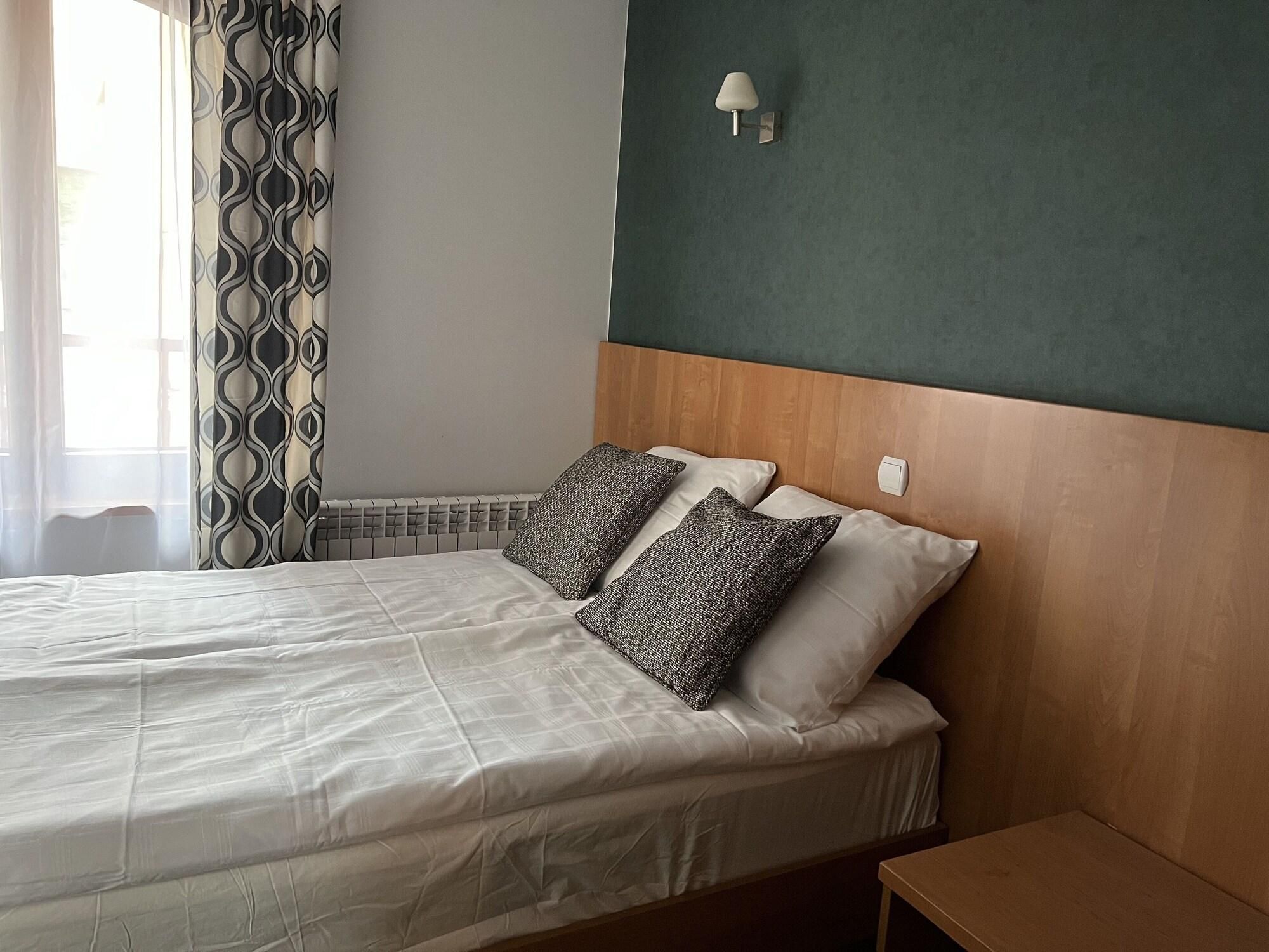 Una cama bien hecha con edredón blanco y almohadas estampadas, un cabecero de madera y una mesita de noche pequeña.