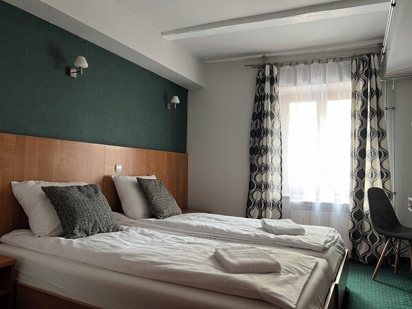 Une chambre d’hôtel avec deux lits, une tête de lit en bois, une table de chevet, une chaise et une fenêtre avec des rideaux à motifs.