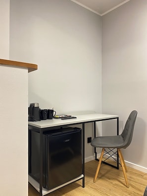 Uma cozinha compacta com geladeira, cafeteira e uma pequena mesa.