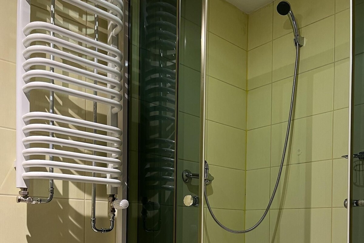 A glass-enclosed shower with a handheld showerhead and a towel rack with white towels.