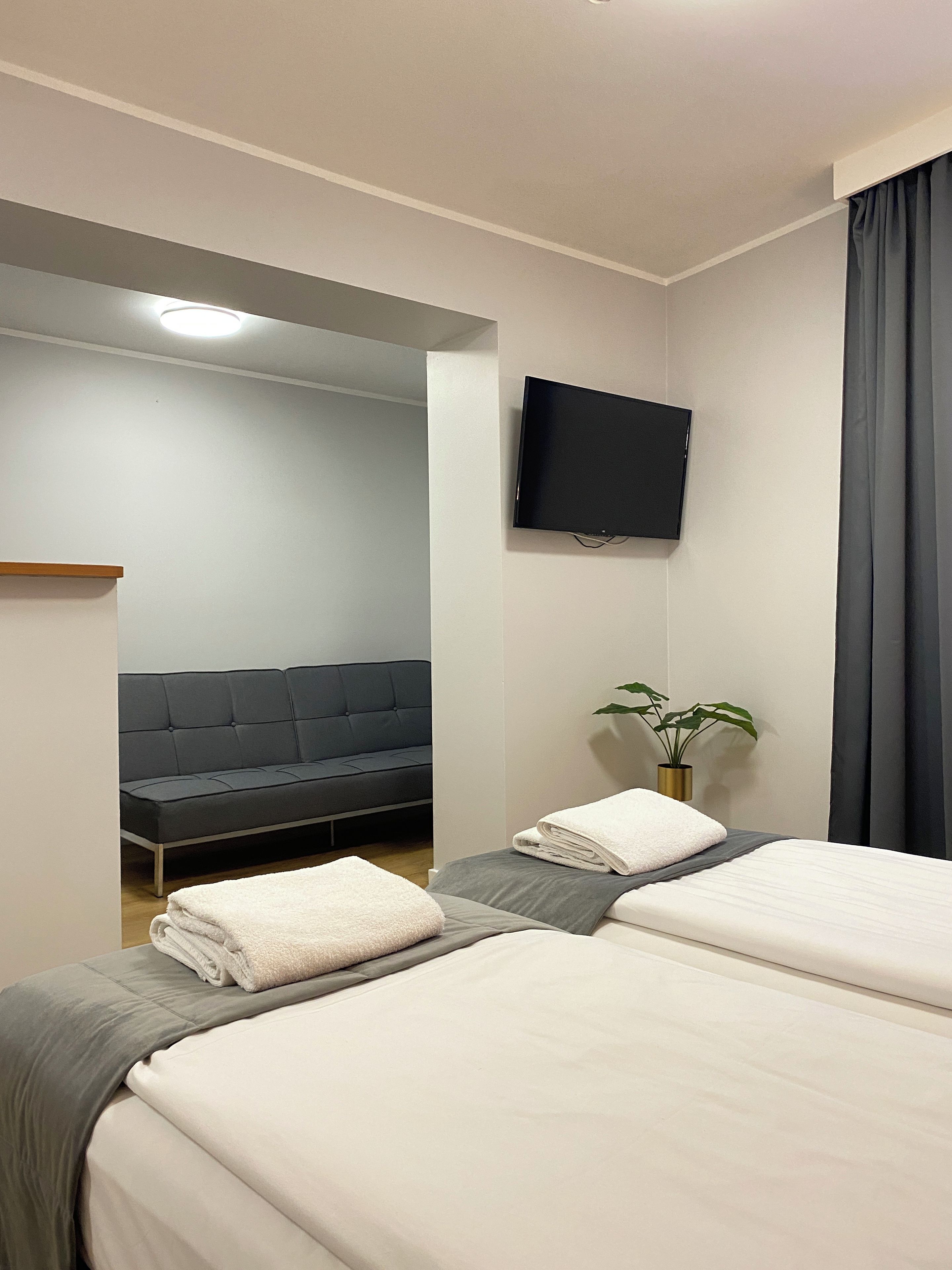 A hotel room with two beds, a flat-screen TV, a sofa, and a potted plant.
