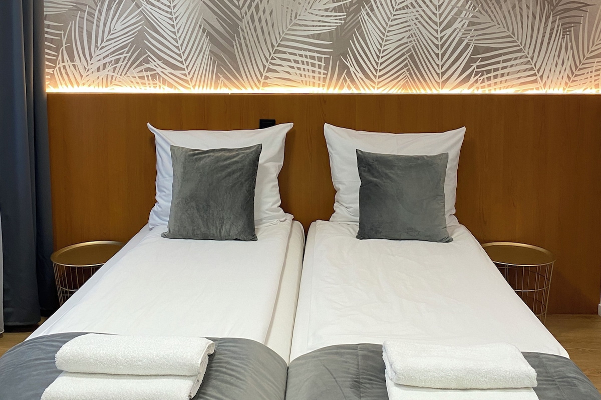A double bed with white and gray bedding, two pillows, and folded towels.