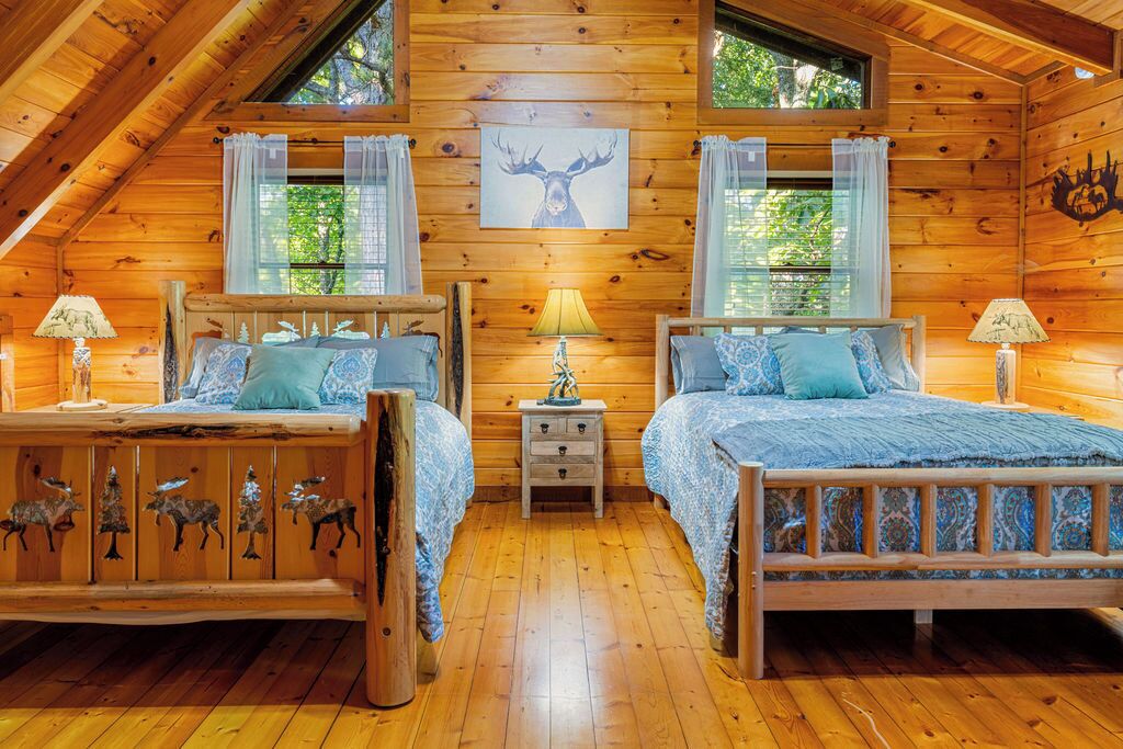 Una cabaña con dos camas de madera, una mesita de noche, una lámpara y un adorno de pared con motivos de ciervo.