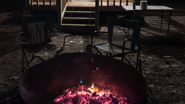 Une petite cabane avec un foyer, des sièges d’extérieur et des guirlandes lumineuses.