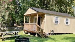 Une petite cabane à un seul étage, dotée d’un porche, d’une table de pique-nique et d’un foyer.