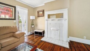 A living room with a beige wall, a white fireplace, a beige sofa, and a glass coffee table. - Downtown Home Conveniently Located (Macon)