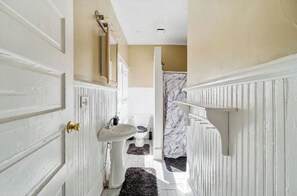 Un couloir étroit avec une porte blanche, un lavabo blanc et un espace de douche en marbre.