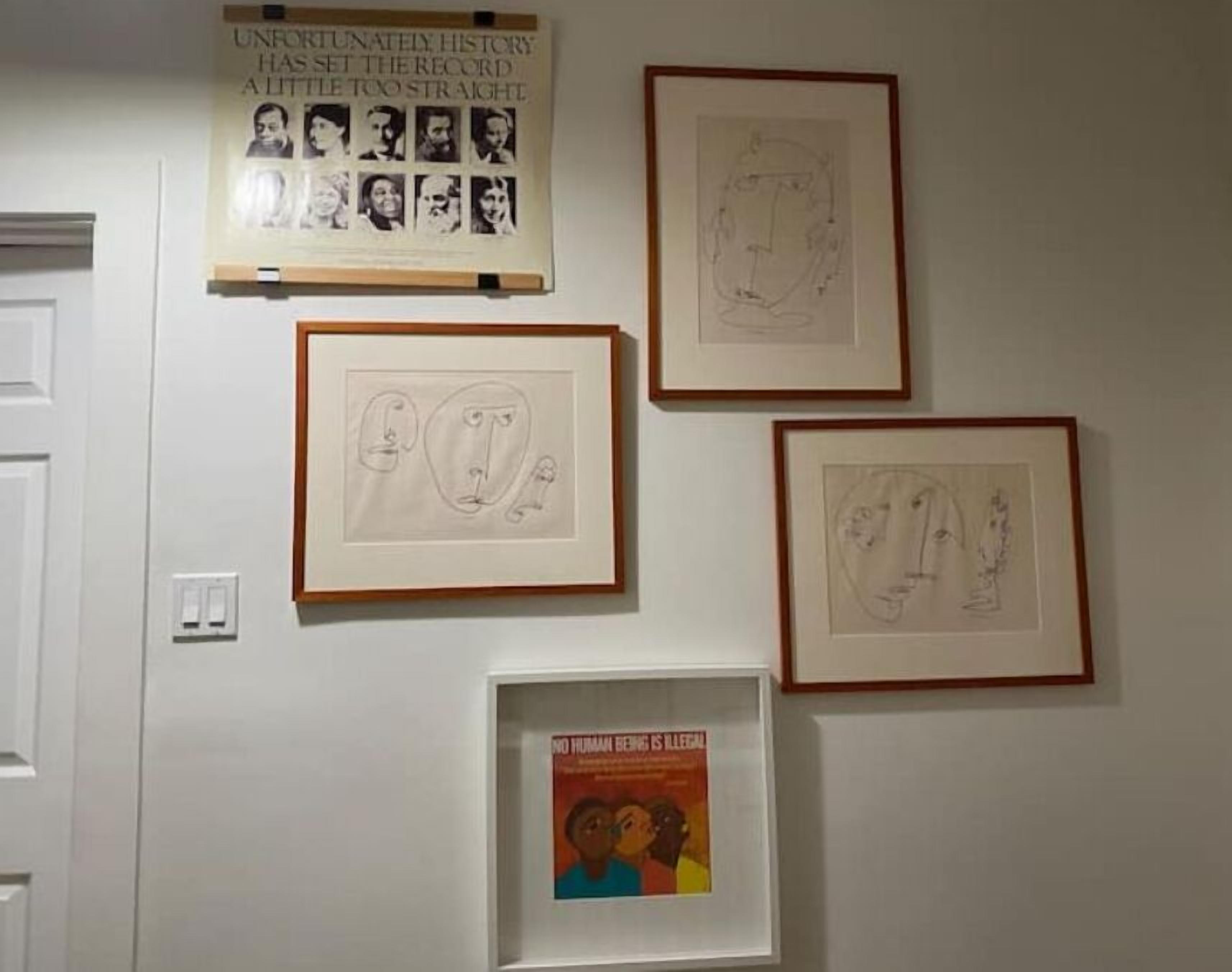 Una pared con obras de arte enmarcadas, incluyendo un cartel y bocetos.