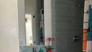 A bathroom with a white sink, a mirror, a potted orchid, and a shower with a striped curtain.