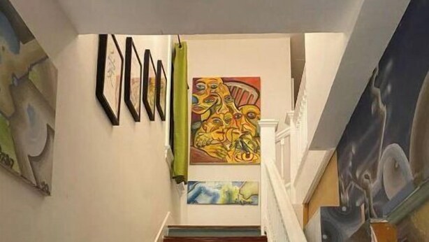 A staircase with colorful steps leading to a landing with framed artwork and a painting.