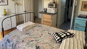 Een compacte slaapkamer met een bed, nachtkastje en een klein keukenhoekje.