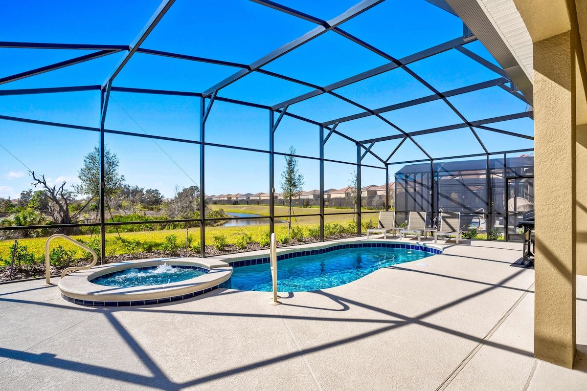 A covered outdoor swimming pool with a hot tub, surrounded by a clear view of a natural landscape.