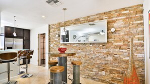 Una cocina moderna con protector de piedra en la pared, un espejo grande y una zona de bar con taburetes.