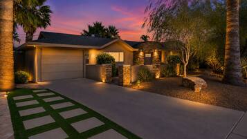A modern house with a garage, stone accents, and a well-lit driveway at dusk.