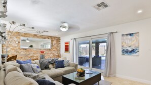 Una sala moderna con un conjunto de sofá, una mesa de centro con fruta, un espejo grande y vistas al exterior a través de una puerta corrediza de vidrio.