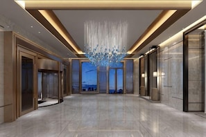 A spacious lobby with a modern chandelier, elevators, and a view through large glass doors. - Ya Le Xuan Hotel (Shehong)