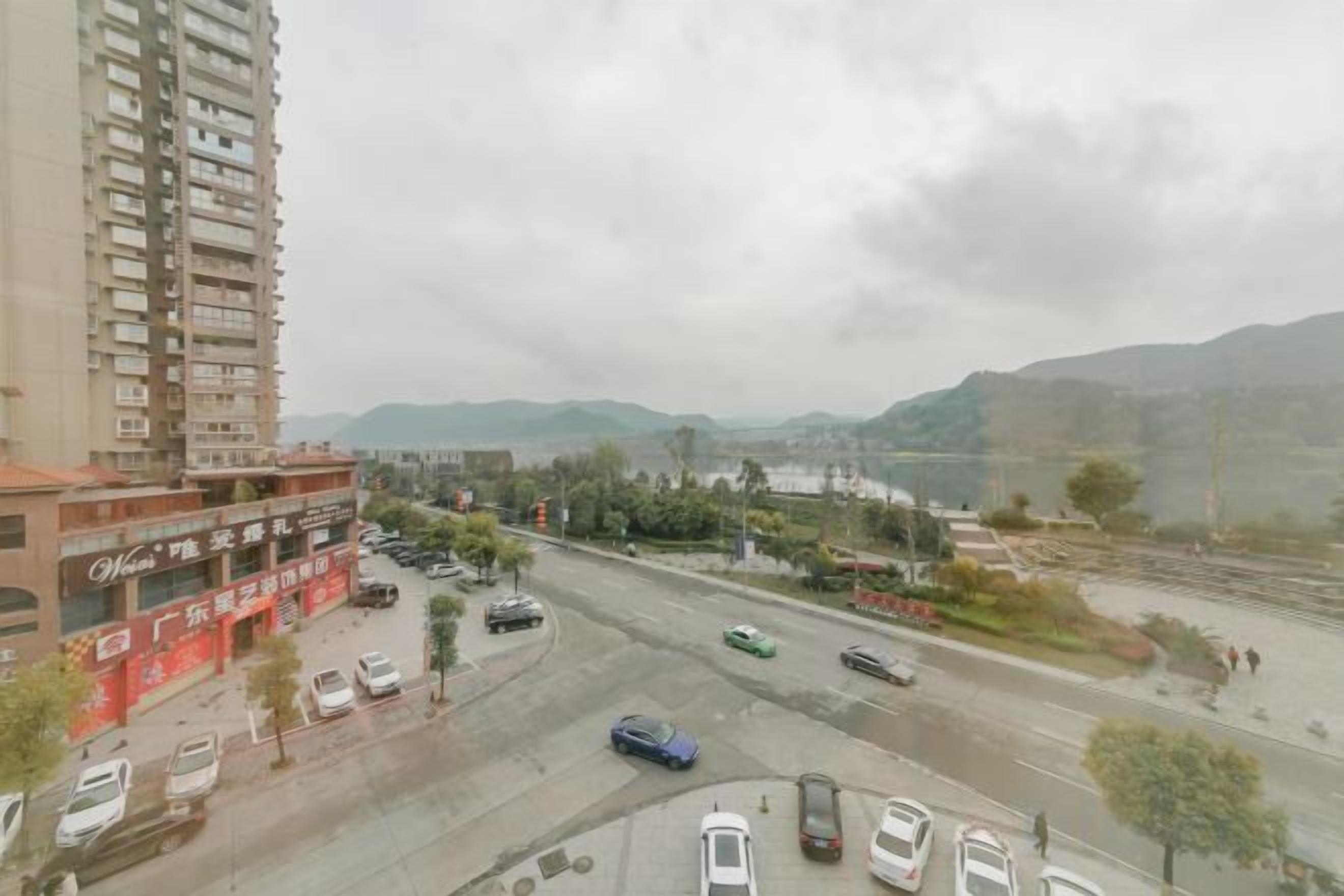 Un edificio de varios niveles con una planta baja comercial, un estacionamiento y una carretera con vehículos.