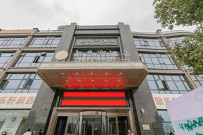 A hotel entrance with a modern facade, large glass windows, and a prominent entrance with a red accent. - Ya Le Xuan Hotel (Shehong)