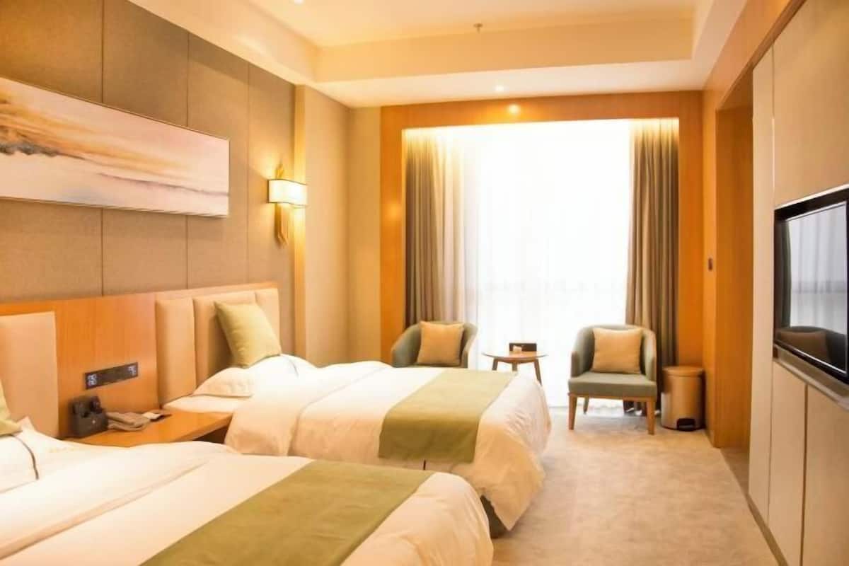 A hotel room with two beds, a television, a desk, and a chair.