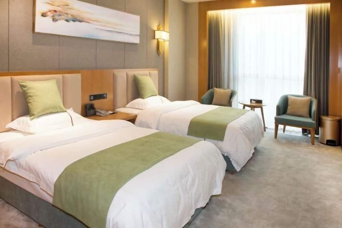 A hotel room with two beds, a nightstand, a chair, and a large window with curtains.