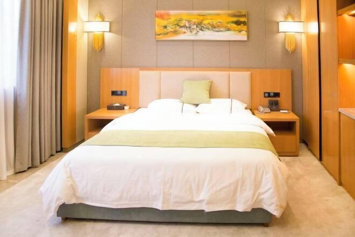 A hotel room with a large bed, two bedside tables, a painting on the wall, and a lamp on each side of the bed.