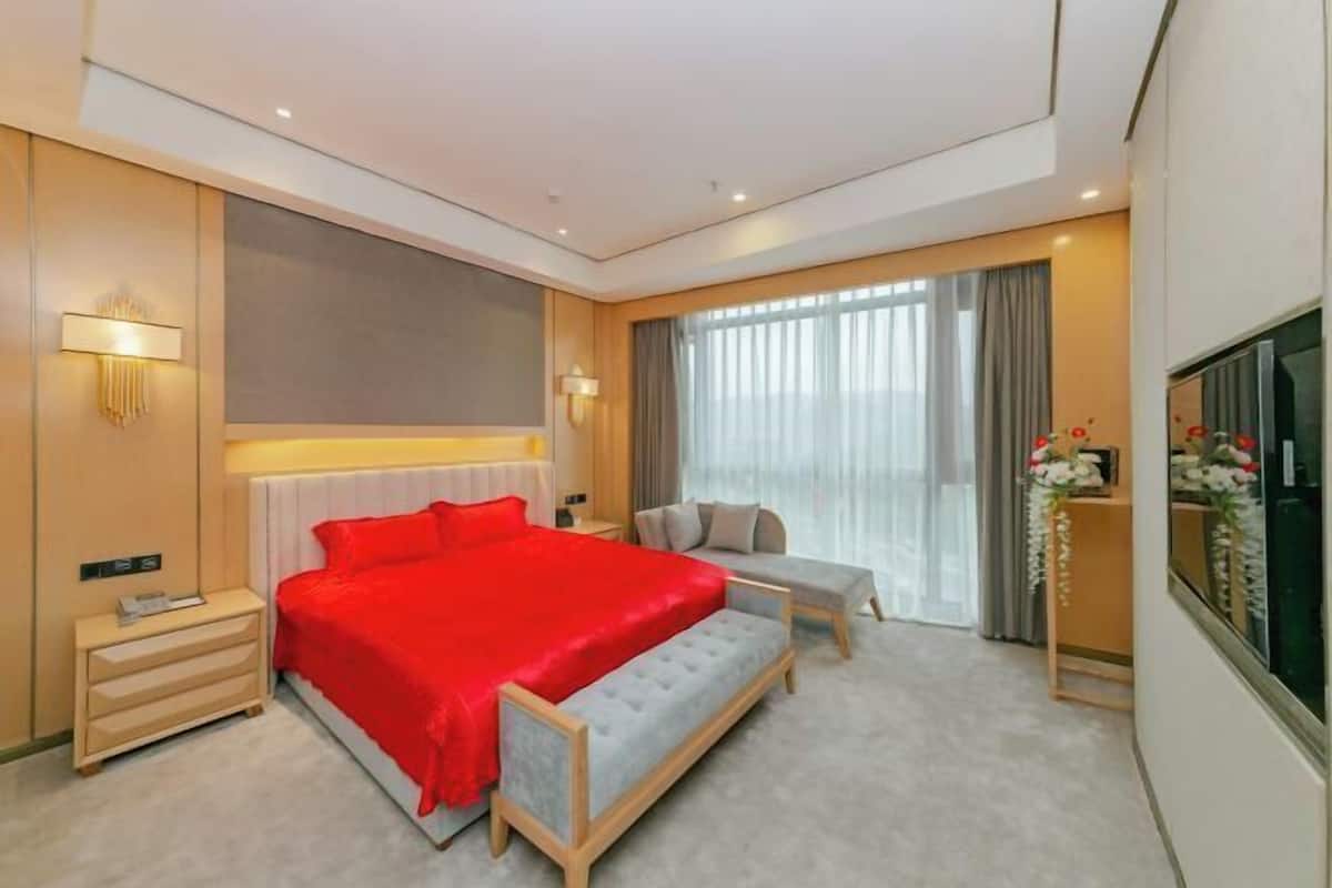 A modern hotel room with a large bed, a bench, a bedside table, a TV, and a window with curtains.