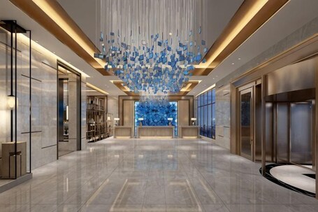 A spacious lobby with a modern chandelier, a reception desk, and a large blue wall feature.. Ya Le Xuan Hotel