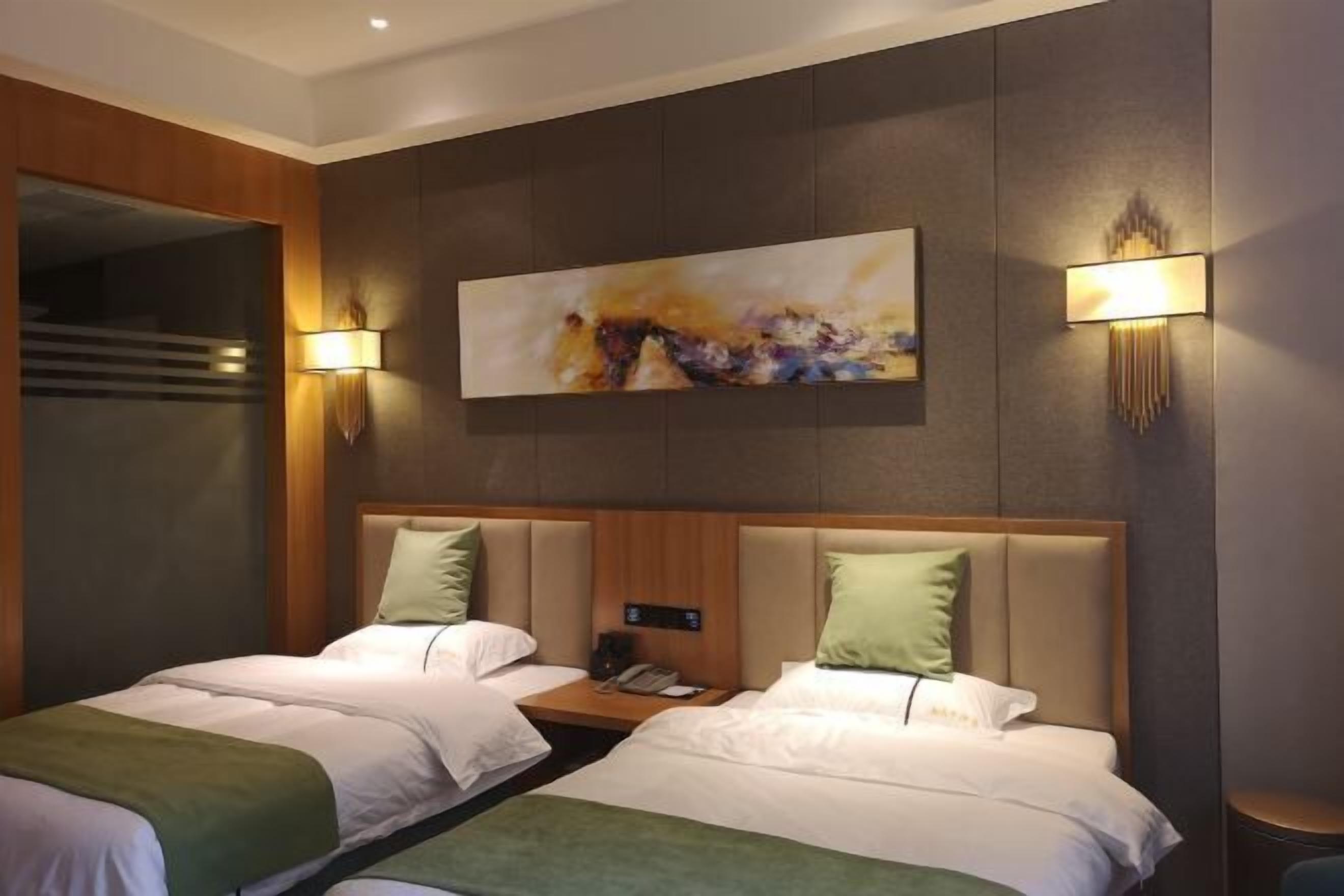 A hotel room with two beds, a painting on the wall, and two wall-mounted lamps.