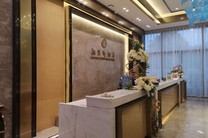 A reception desk with a marble top, a floral arrangement, and a sign with text. - Ya Le Xuan Hotel (Shehong)