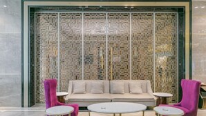 A modern interior with a patterned wall, a sofa, and two round tables with chairs. - Ya Le Xuan Hotel (Shehong)