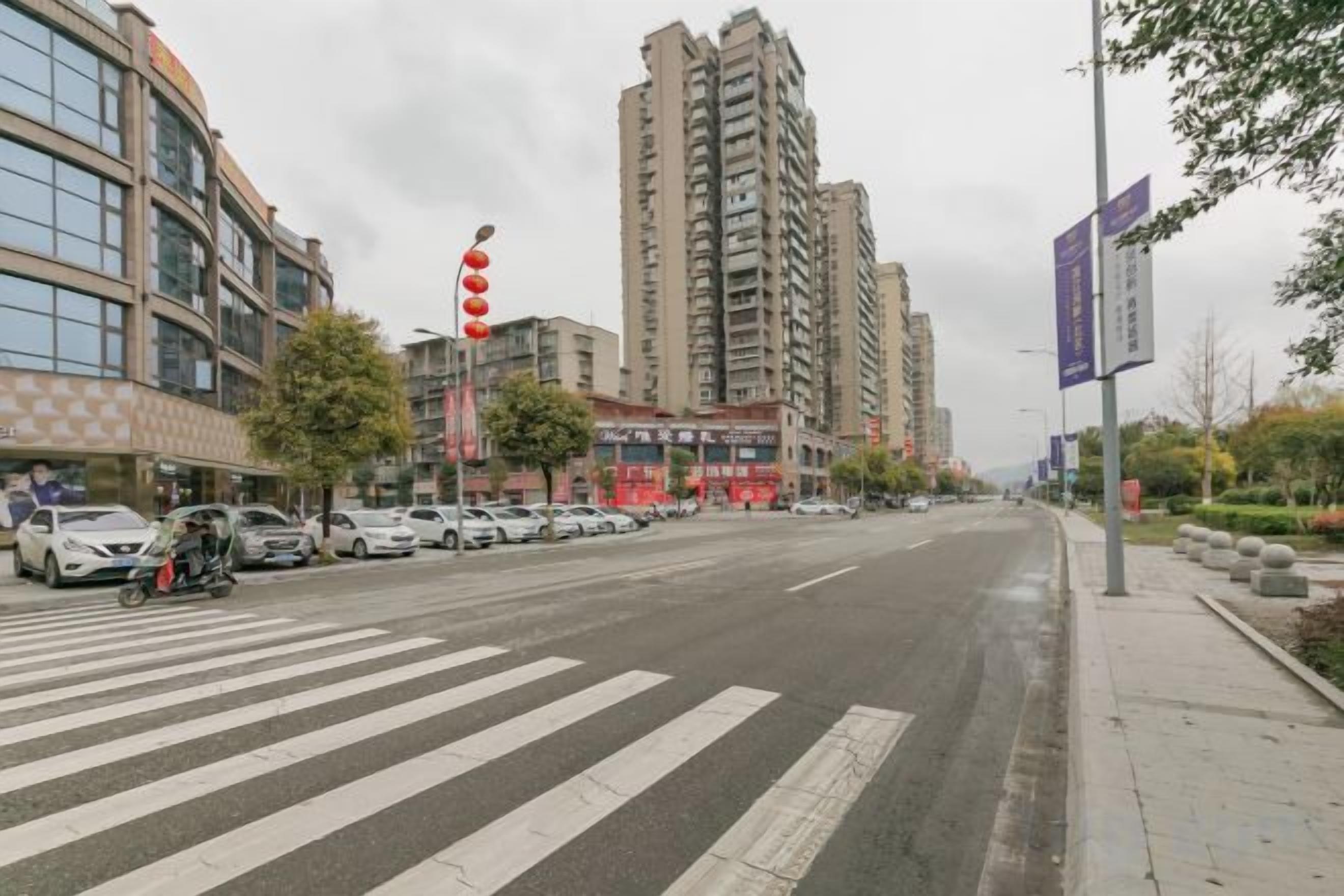 A wide street with a pedestrian crossing, tall buildings, and parked cars.