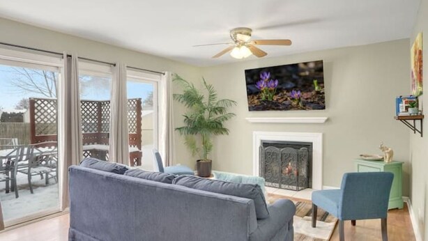 A living room with a gray sofa, a blue chair, a fireplace, and a ceiling fan. - PROMO 10% WEEKLY AND 15% MONTHLY OFF
Naperville/Aurora, King Bed, Fenced Yard! (Aurora)