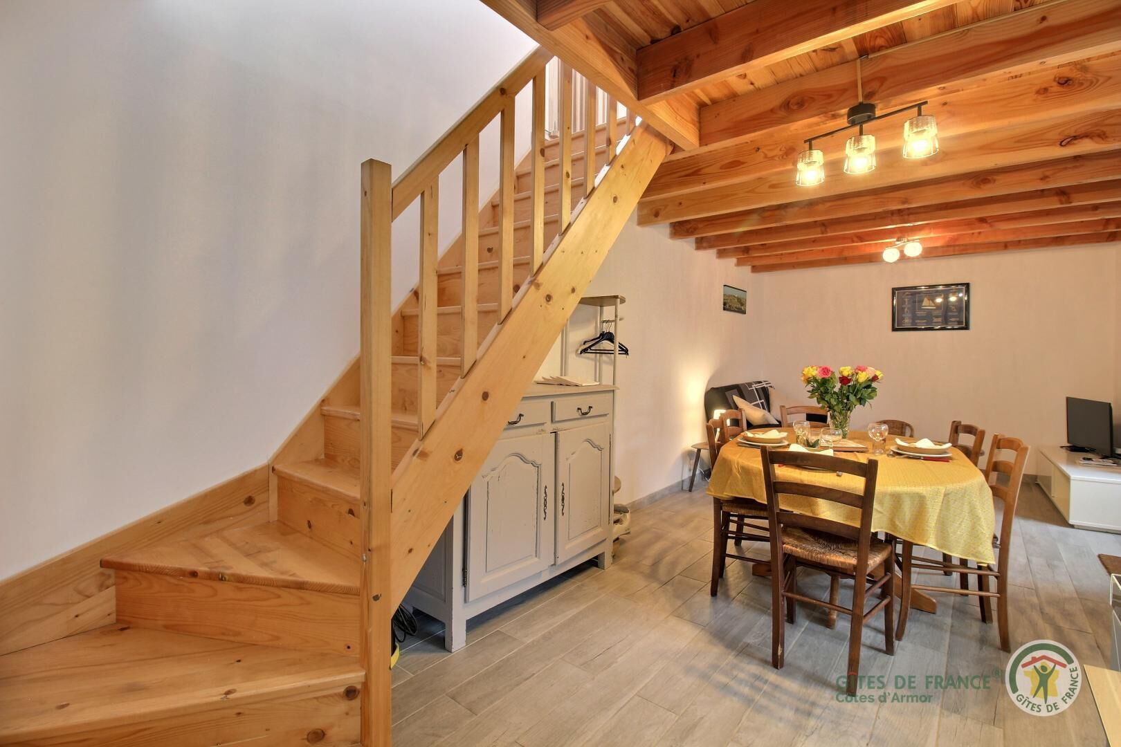 A wooden staircase leading to a dining area with a table set for four, a white cabinet, and a hanging light fixture above the table.