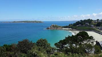 A coastal view with a sandy beach, rocky outcrops, and a lighthouse.
