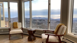 A spacious room with large windows offering a mountain view. There are two armchairs and a wooden coffee table. - Amazing Mountain View’s from every room! Hot Tub/3 Fire pits & Game Rm (Windham)