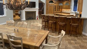 A spacious kitchen with a large island, wooden bar stools, and a fireplace. - Amazing Mountain View’s from every room! Hot Tub/3 Fire pits & Game Rm (Windham)