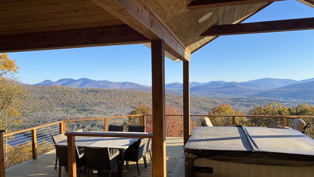 A wooden deck with a table and chairs, a hot tub, and a view of mountains. - Amazing Mountain View’s from every room! Hot Tub/3 Fire pits & Game Rm (Windham)