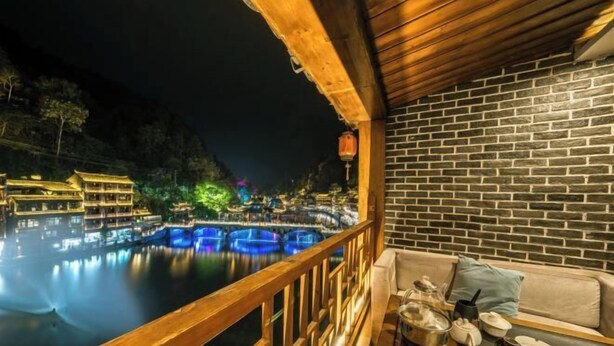 A balcony with a wooden railing overlooking a water body with illuminated structures. - Fenghuang Fanyin Zhenpin Inn (Fenghuang County)