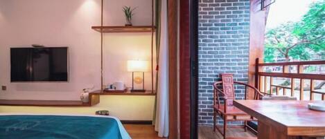 A hotel room with a bed, a TV, a desk with a lamp, and a balcony with a brick wall and wooden railing.