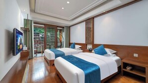 A hotel room with two beds, a TV, a wooden nightstand, and a view of a garden through a glass door. - Fenghuang Fanyin Zhenpin Inn (Fenghuang County)