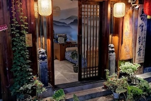 Ein traditioneller japanischer Eingangsbereich mit einer Schiebetür, Topfpflanzen und Blick ins Innere.