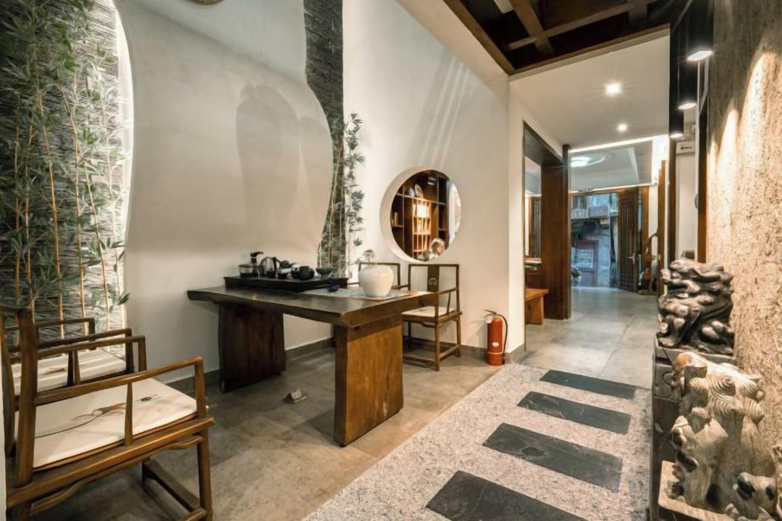 A room with a stone wall, a wooden table, and chairs. There is a mirror on the wall and a plant on the table.