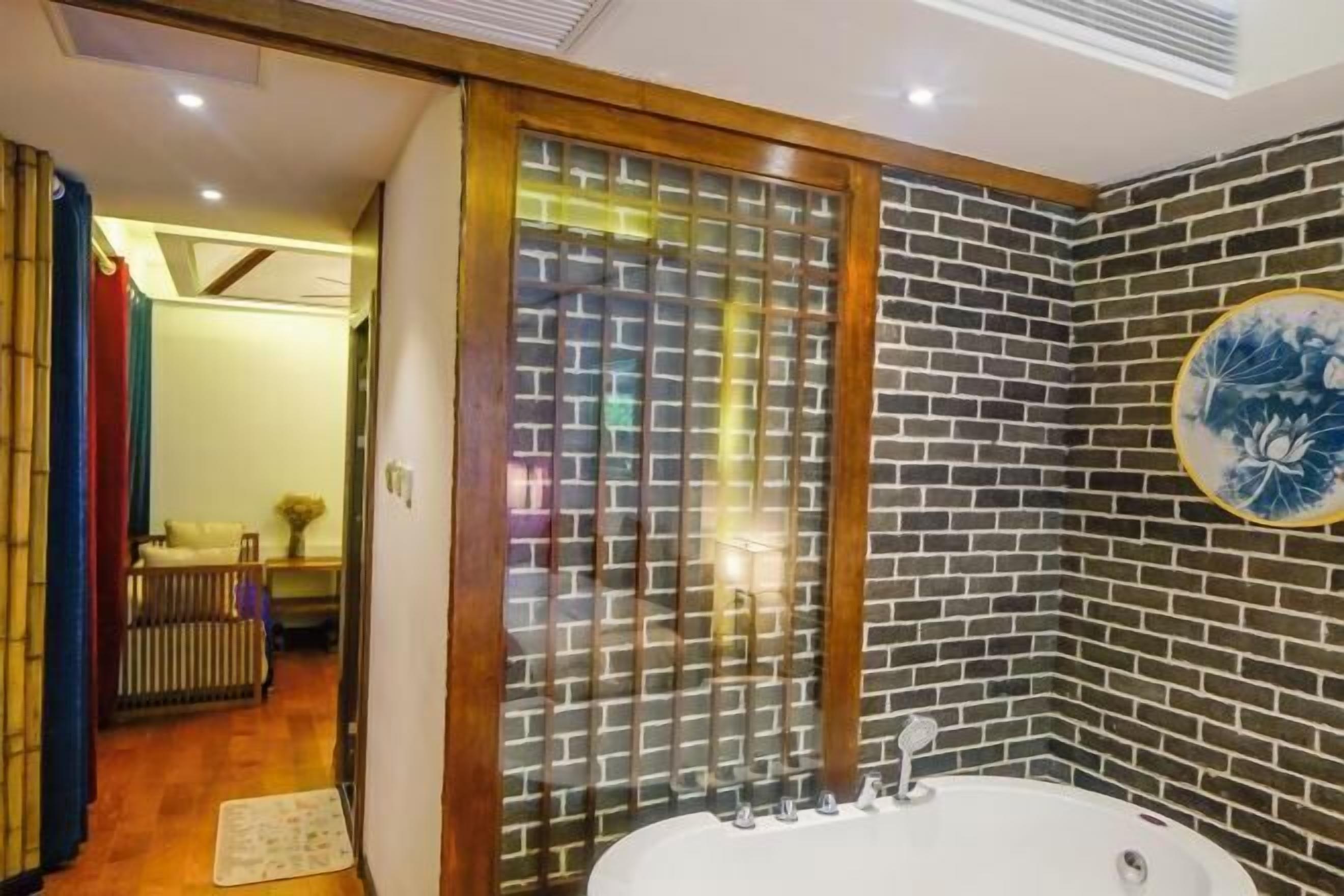 A bathroom with a large bathtub, a wooden-framed glass door, and a brick-patterned wall.